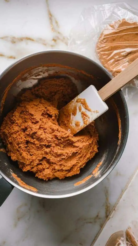 A large mixing bowl with gingerbread dough just combined, a spatula resting on the side