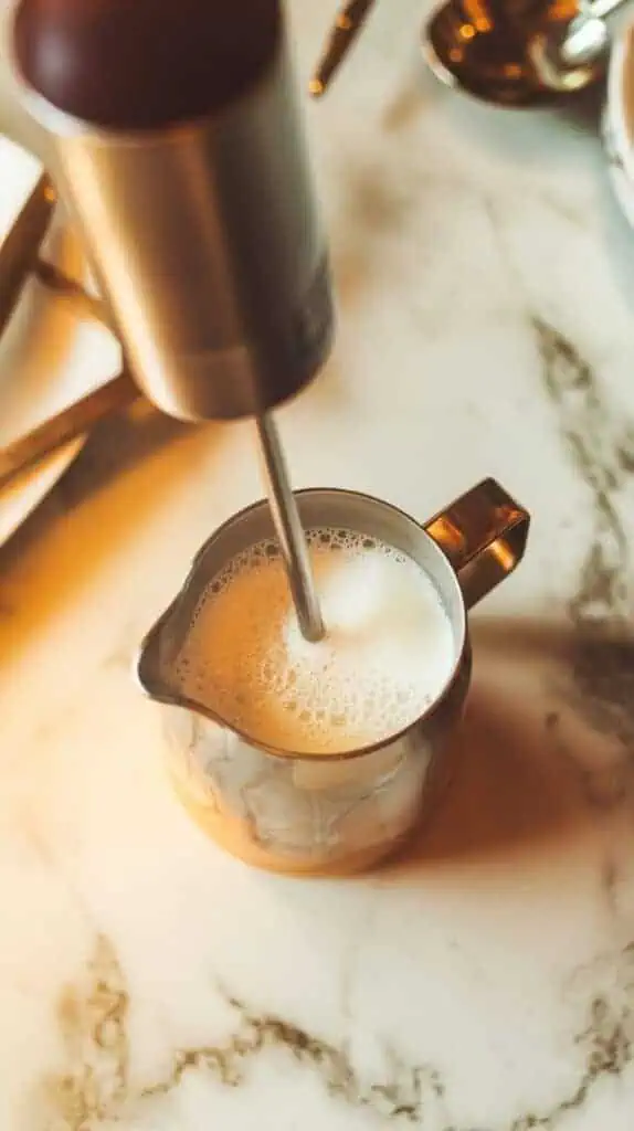 A small pitcher of milk being frothed with a handheld frother