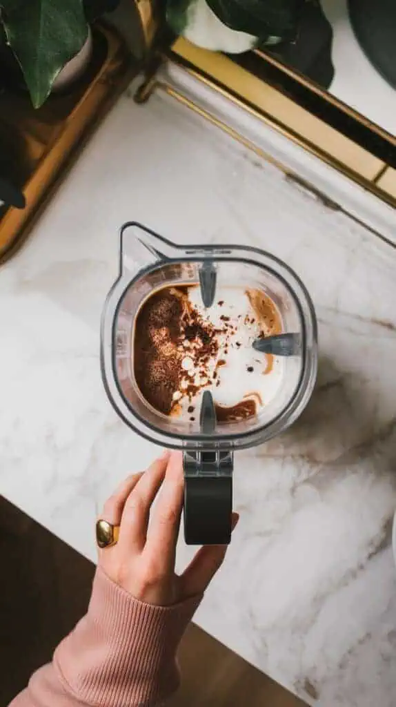 A blender filled with coffee, frothed milk, and white chocolate mixture being blended together.