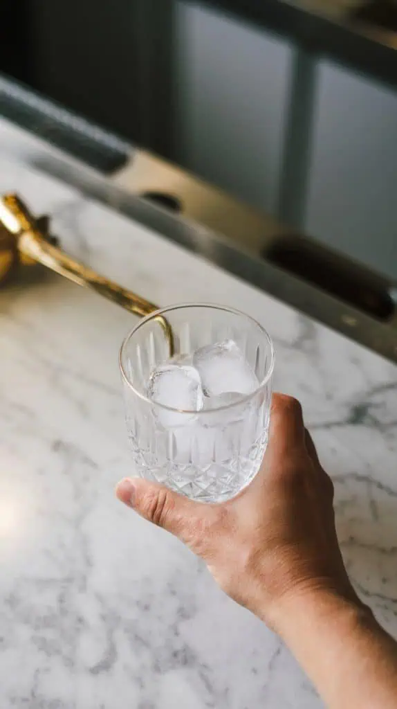 A short cocktail glass filled with ice cubes on a white marble counter with hints of gold