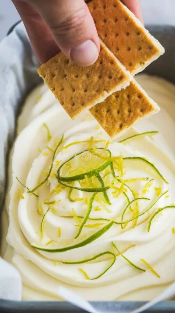 A super close-up, top-down shot of crushed graham crackers and fresh lime zest being sprinkled over the fudge