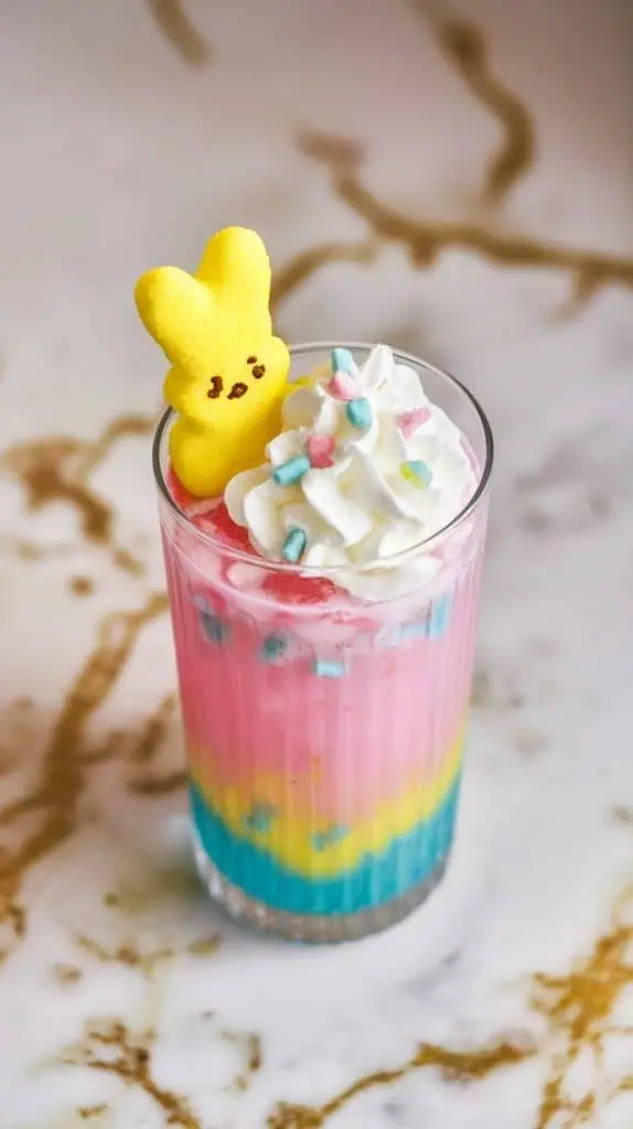 a bright yellow marshmallow Peep resting on top of a whipped cream-topped punch, with pastel sprinkles scattered over the creamy surface