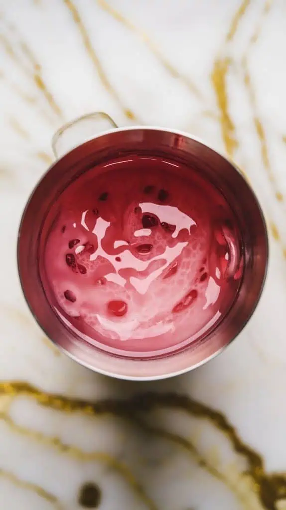 a cocktail shaker filled with creamy half-and-half, deep pink watermelon schnapps, clear vanilla vodka, and a drizzle of pink Starburst syrup