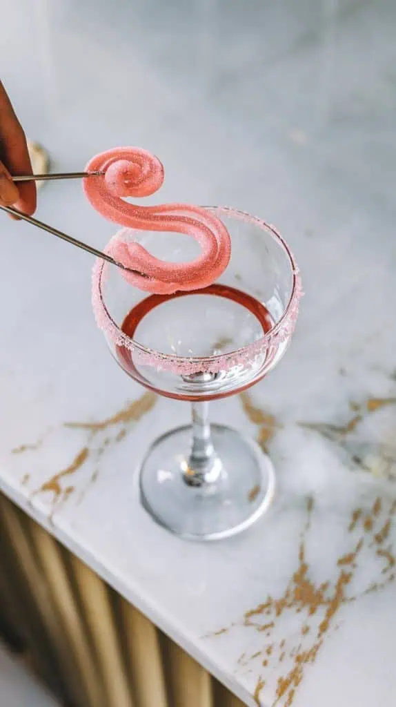 a martini glass rim being dipped into a small plate of water, followed by a swirl in pink sugar, creating a sparkling, candy-coated edg