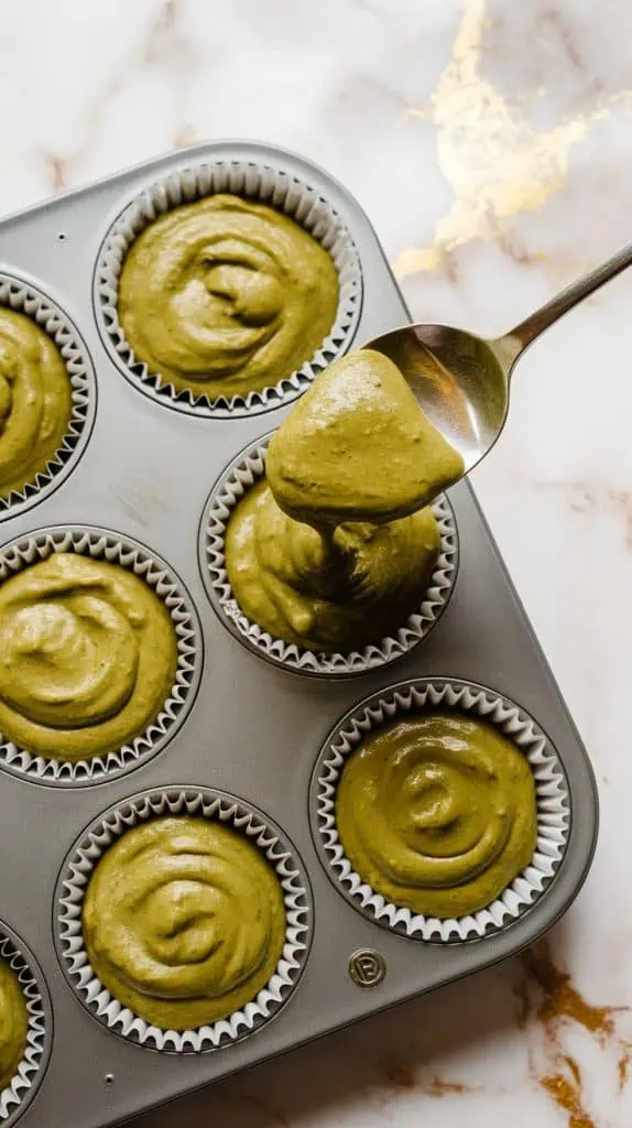 a muffin tin lined with paper liners, each cup filled with thick greenish matcha banana batter