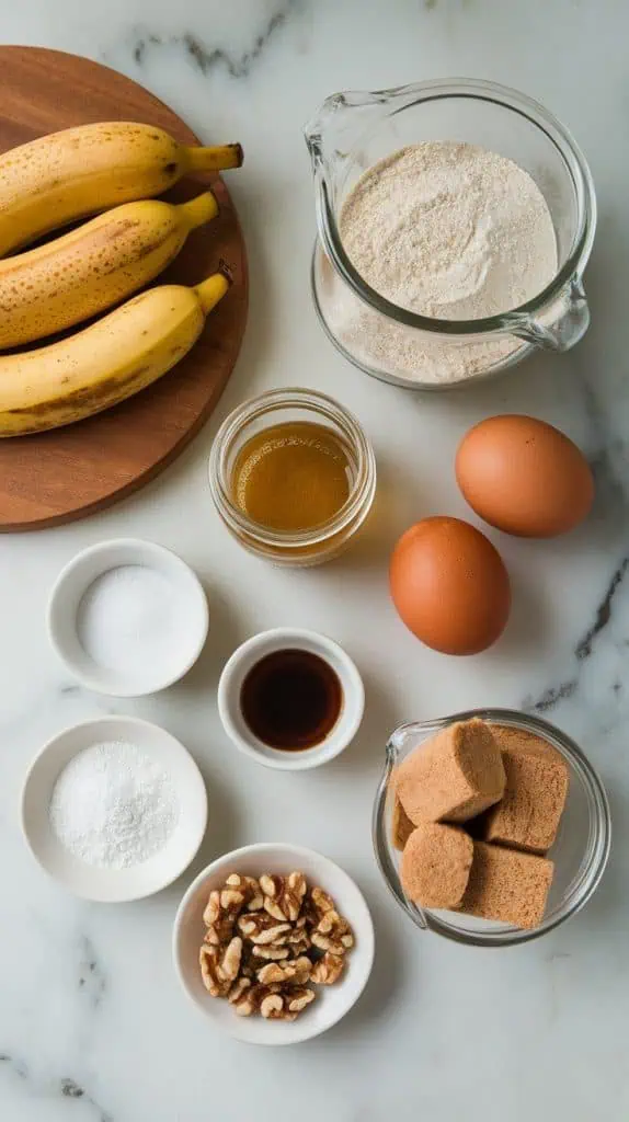 all ingredients for brown sugar banana nut muffins arranged on a white marble countertop with hints of gold. The ripe bananas are slightly speckled and placed on a wooden board.