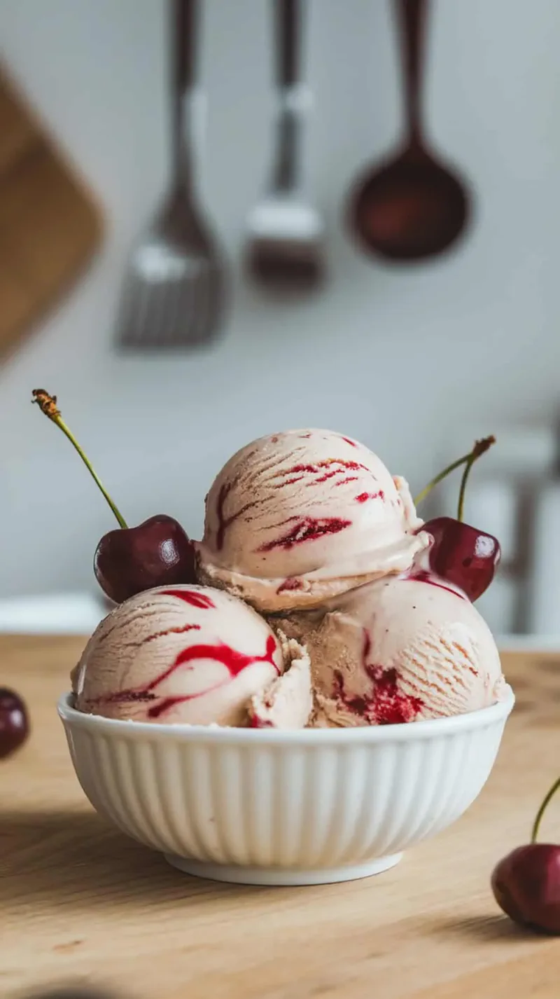 Cherry ripple coffee ice cream in a white bowl with cherries on top.