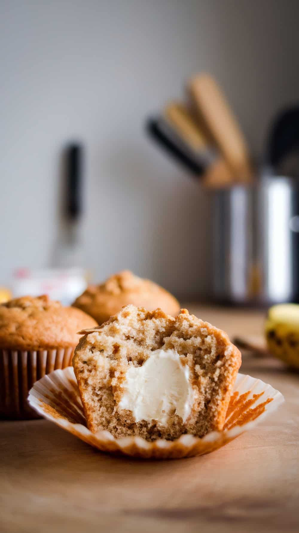 Delicious banana cream cheese muffins with a bite taken out, showcasing the creamy filling inside.