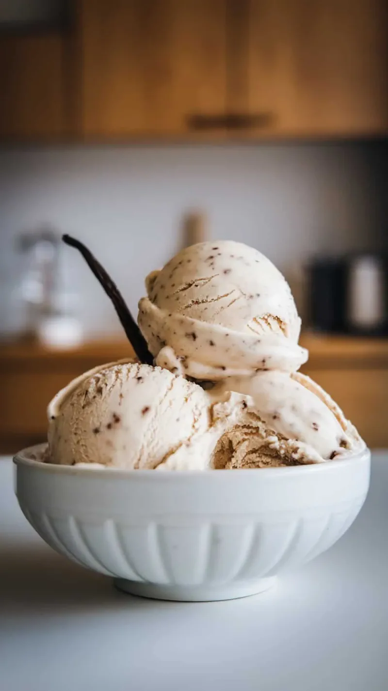A bowl of vanilla bean coffee ice cream with scoops and a vanilla bean stick.