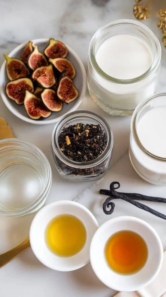 ingredients for fig vanilla milk tea: chopped dried figs on a small white plate, black tea in a tiny white dish, water in a clear glass jar, milk in a second clear glass jar, vanilla extract on a small white plate, and honey on another small white plate
