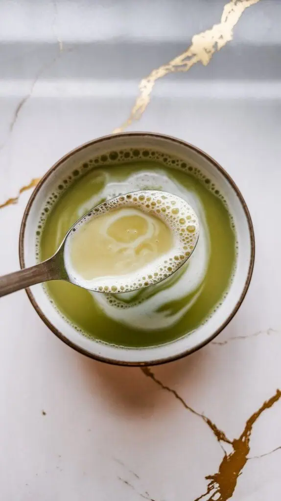 coconut milk being stirred into green tea, creating pale green swirls and a smooth creamy blend.