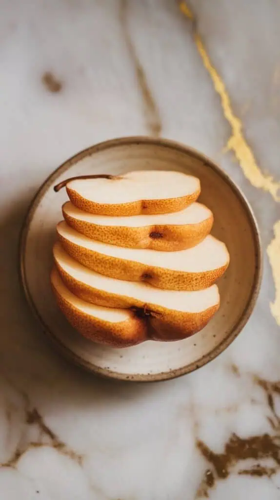 a peeled ripe pear cut into thin slices, arranged neatly on a small ceramic plate, with the peel curled beside it