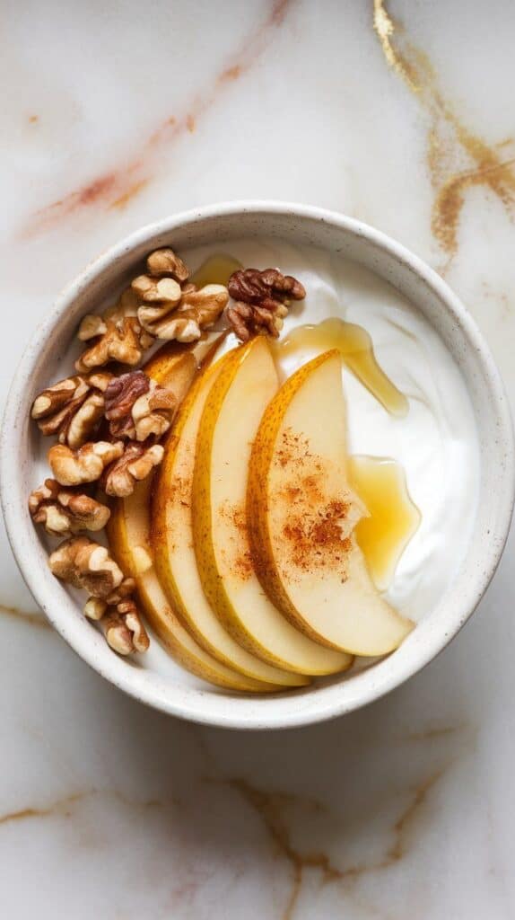 a finished ginger pear yogurt bowl with creamy yogurt, golden pear slices, chopped walnuts, a drizzle of honey, and a dusting of cinnamon