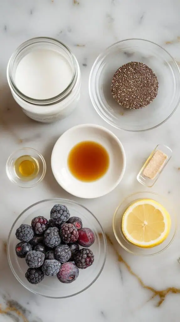  1 cup canned coconut milk in a small clear jar, ¼ cup chia seeds in a clear shallow dish, 1 tablespoon maple syrup on a small white plate, ½ teaspoon vanilla extract on a tiny clear saucer, 1 cup fresh or frozen mulberries in a clear bowl, 1 tablespoon honey in a small plate, and 1 teaspoon lemon juice in a tiny clear dish