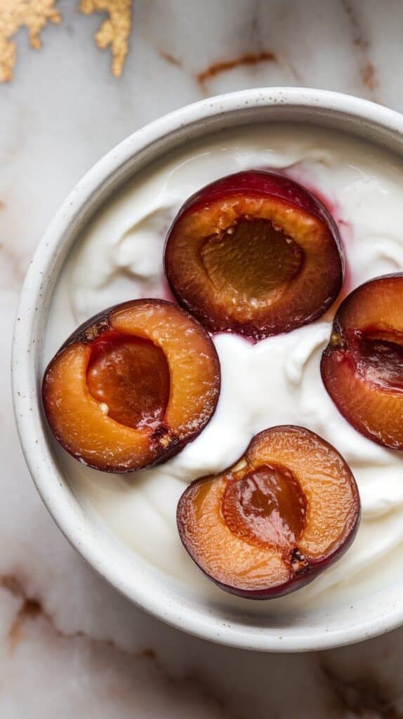 caramelized plum halves gently placed on top of creamy Greek yogurt, juices slightly blending into the yogurt base