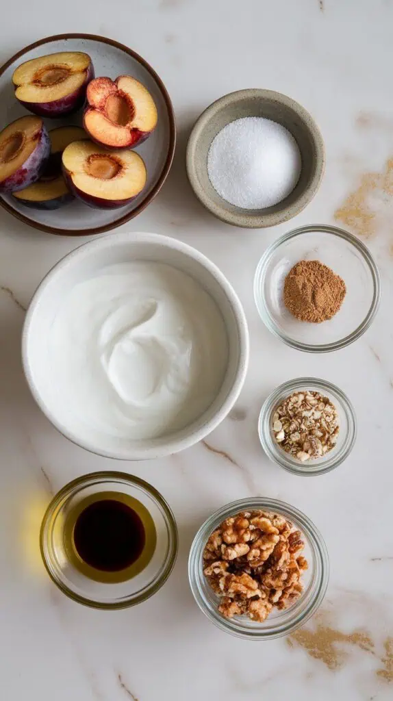  roasted plum yogurt bowl ingredients: ripe plum halves with pits removed on a small plate, Greek yogurt in a shallow dish, coconut sugar on a tiny ceramic plate, ground cinnamon on a small dish, olive oil in a shallow glass plate, balsamic glaze poured into a small plate, and optional toppings—chopped walnuts, hemp seeds, granola—in tiny clear glass jars