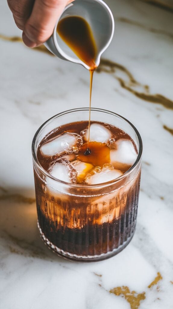vanilla extract being drizzled into a fizzy drink over ice, tiny ripples forming where the vanilla lands