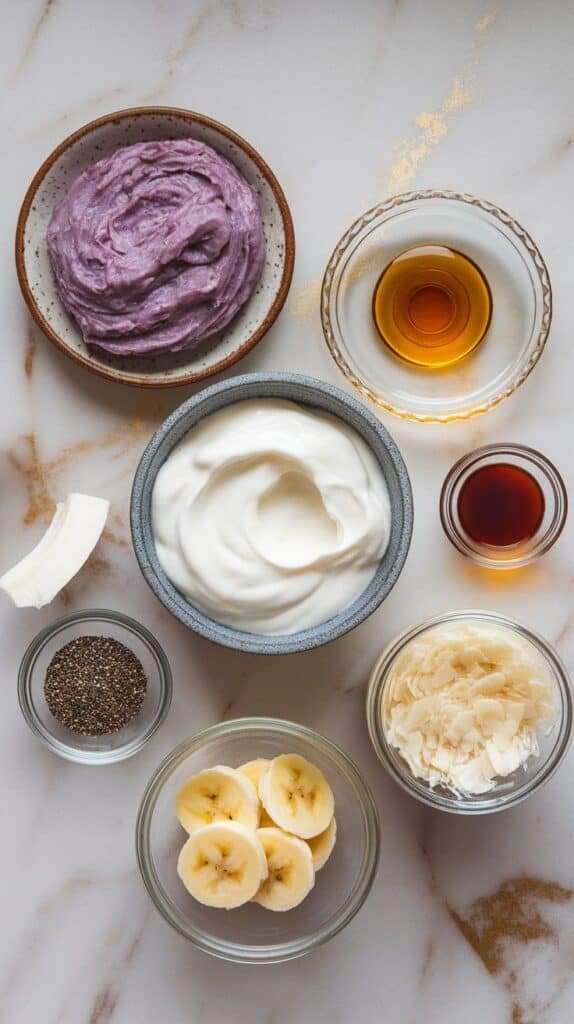 ube coconut yogurt bowl ingredients: creamy mashed ube on a small ceramic plate, thick Greek yogurt in a shallow dish, honey drizzled onto a glass plate, vanilla extract poured into a small dish, shredded coconut in a tiny clear jar, and optional toppings—chia seeds, sliced banana, and coconut milk